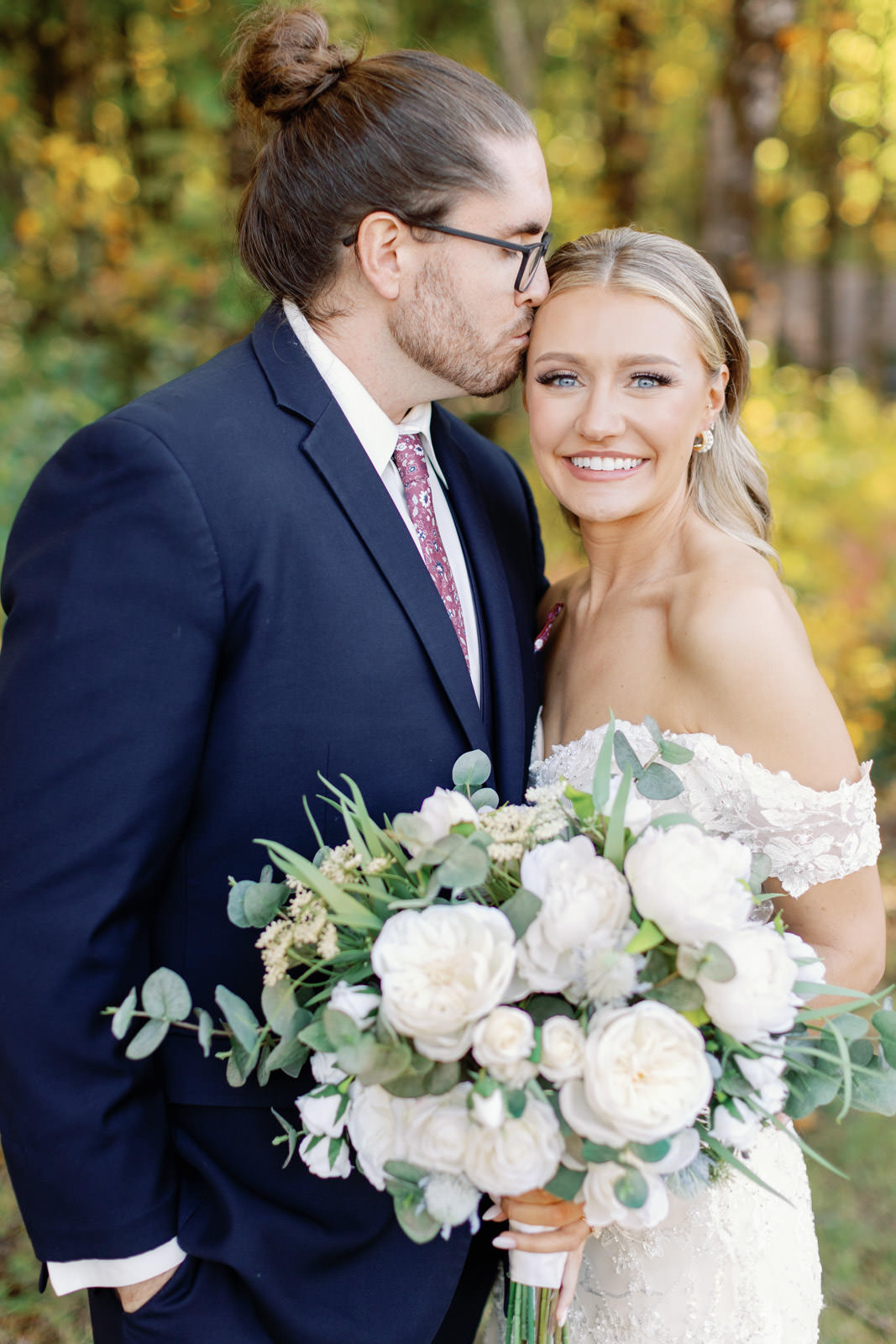 Fall wedding at Stonehurst at Hampton Valley. Couple in wedding attire smiling at the camera while groom kisses bride.