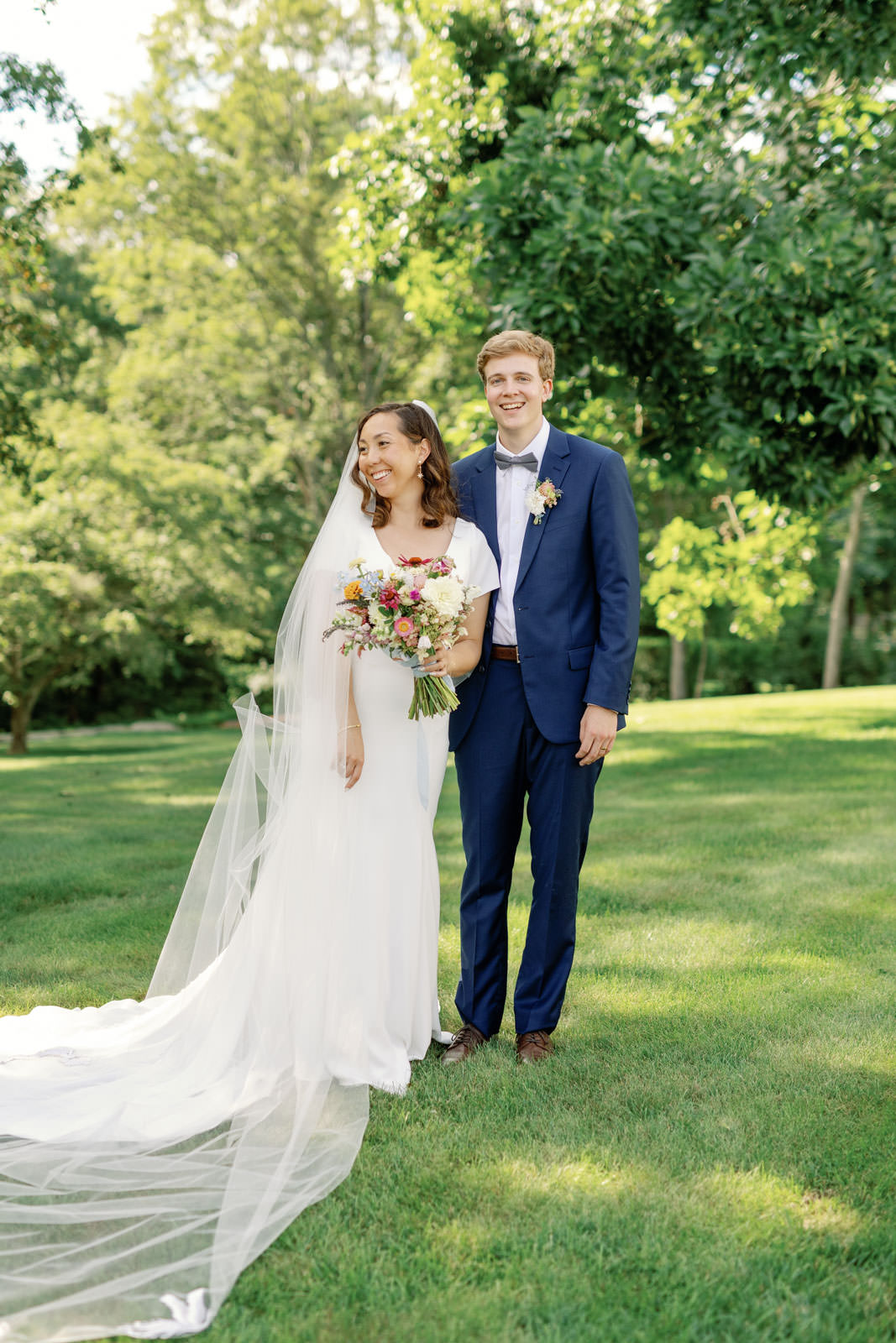 July wedding at Smith Farm Gardens. Couple in wedding attire standing on lawn.