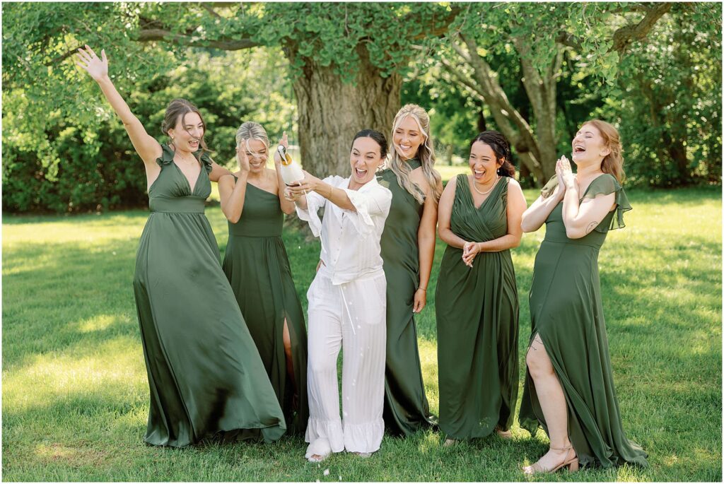 bridesmaids in green popping bottle of champagne on wedding day at summery eolia mansion wedding