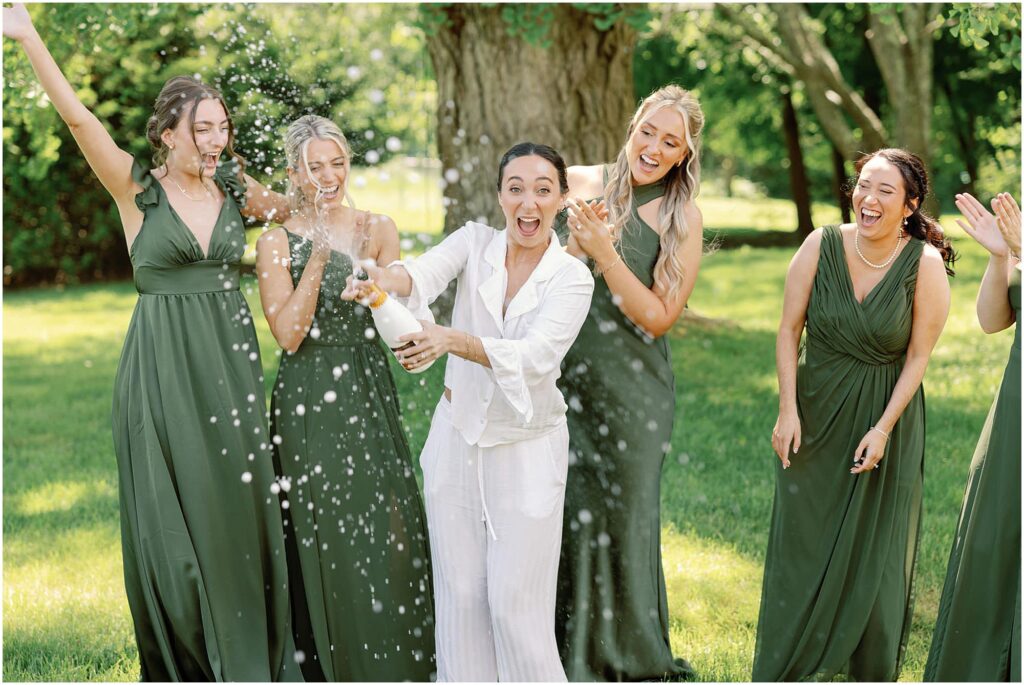 bridesmaids in green dresses popping champagne with bride on wedding day