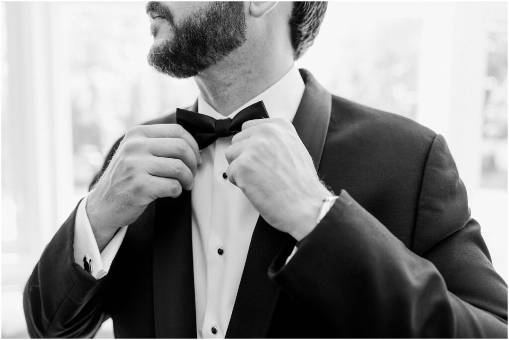 black and white image of groom adjusting his bowtie at his summery eolia mansion wedding