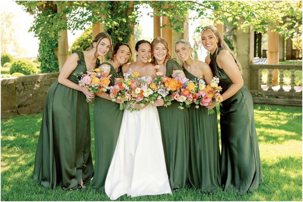 bride in wedding attire surrounded by bridesmaids in green dresses at summery eolia mansion wedding